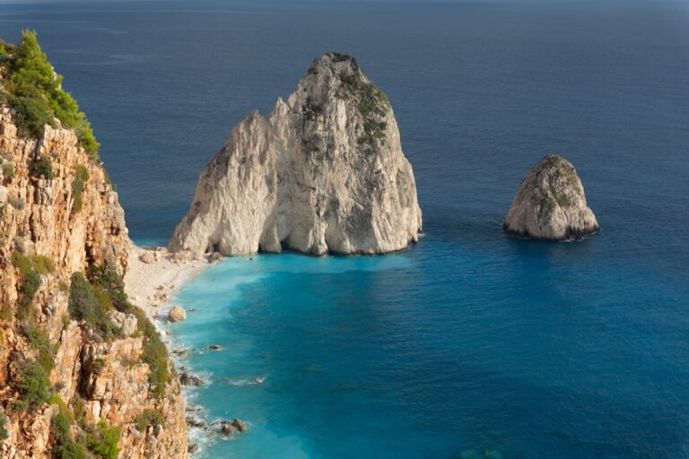 Rocky cliffs overlook a turquoise beach and blue ocean.