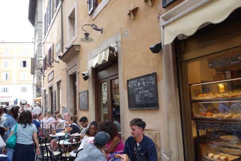 People sit at outdoor cafe tables along a street.